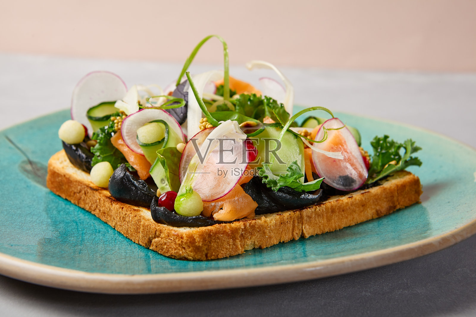 意式烤面包配三文鱼，奶油芝士和蔬菜放在蓝色陶瓷盘子里。现代风格的鲑鱼吐司。现代陶瓷餐具中的鲑鱼意式烤面包。手工制作的餐盘。照片摄影图片