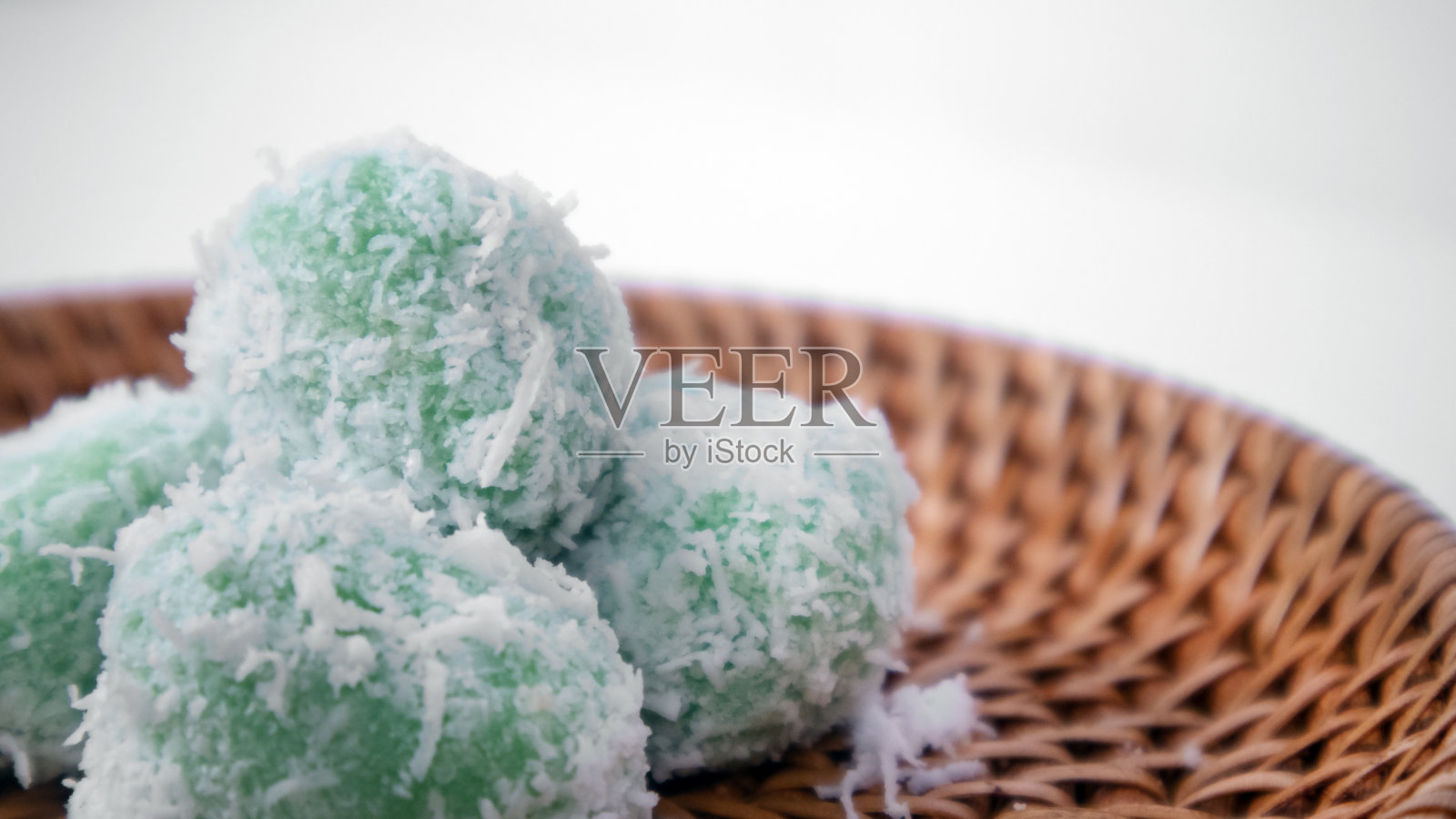 非常接近的上菜或绿色的糯米球，里面充满了液体的棕榈糖，外面裹着磨碎的椰子，背景是白色的照片摄影图片