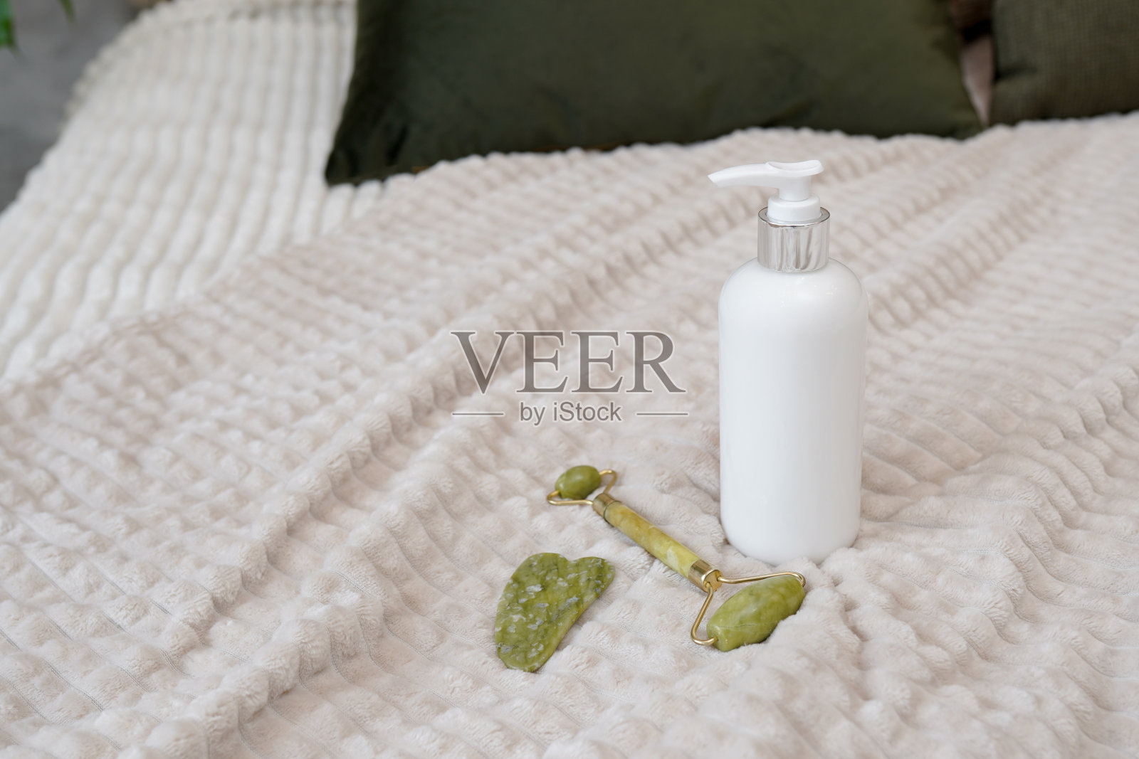 在床上设置家庭面部护理。面部用绿色石英按摩轮或涂砂及美容白瓶保湿乳液进行护肤。化妆品照片摄影图片