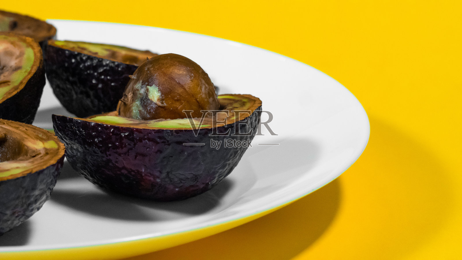 黄色背景坏鳄梨盘子。照片摄影图片