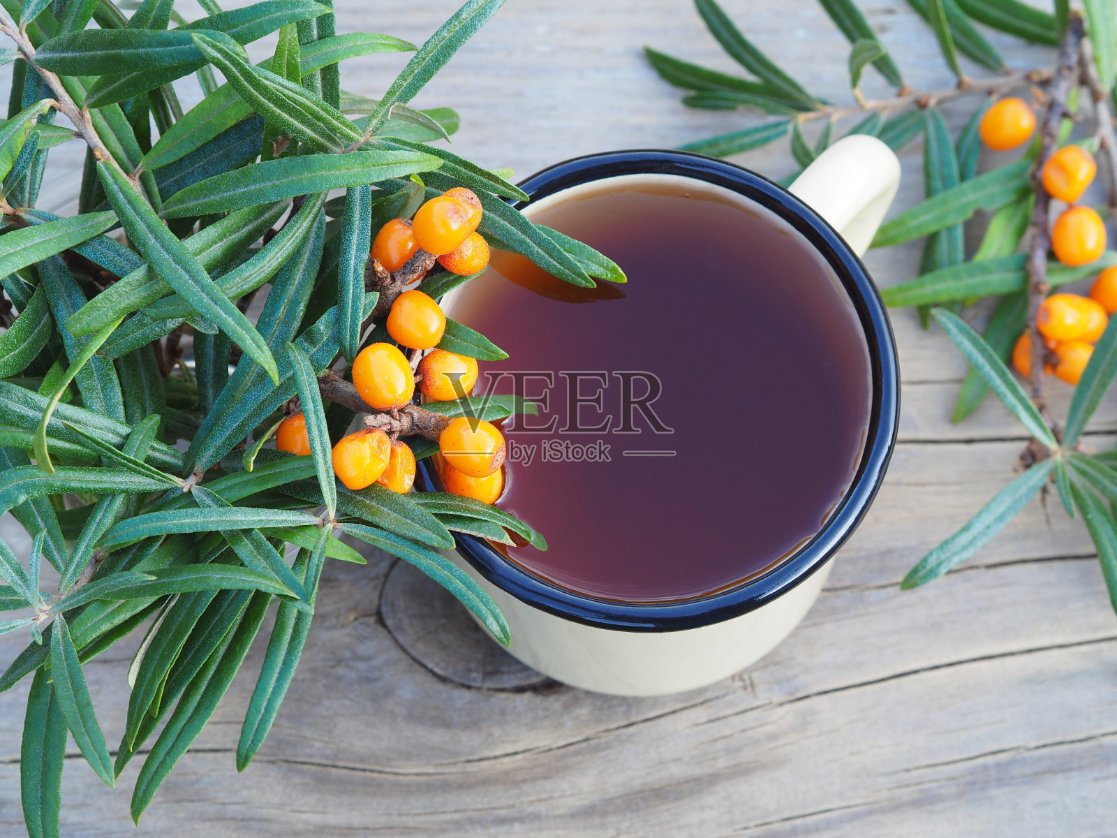 天然饮料与浆果和沙棘枝在一个搪瓷杯木架上，俯瞰。含沙棘果实的健康草本茶照片摄影图片