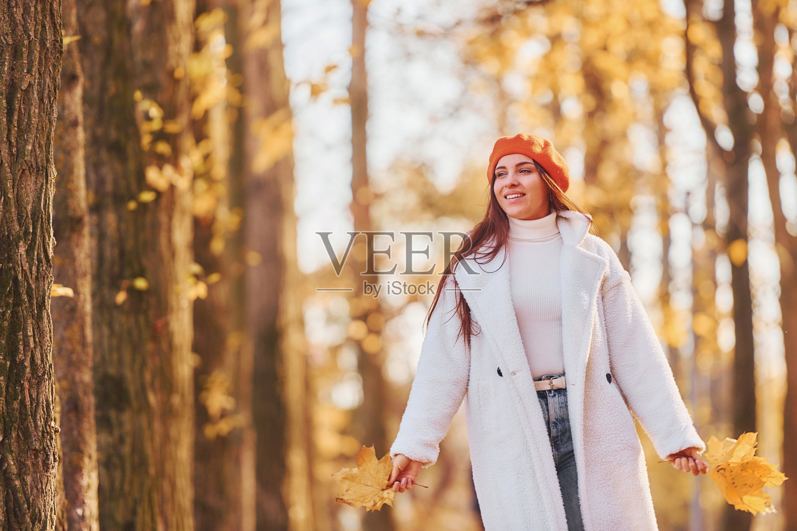 红色贝雷帽。穿着白大褂的女人在秋天的公园里玩耍照片摄影图片