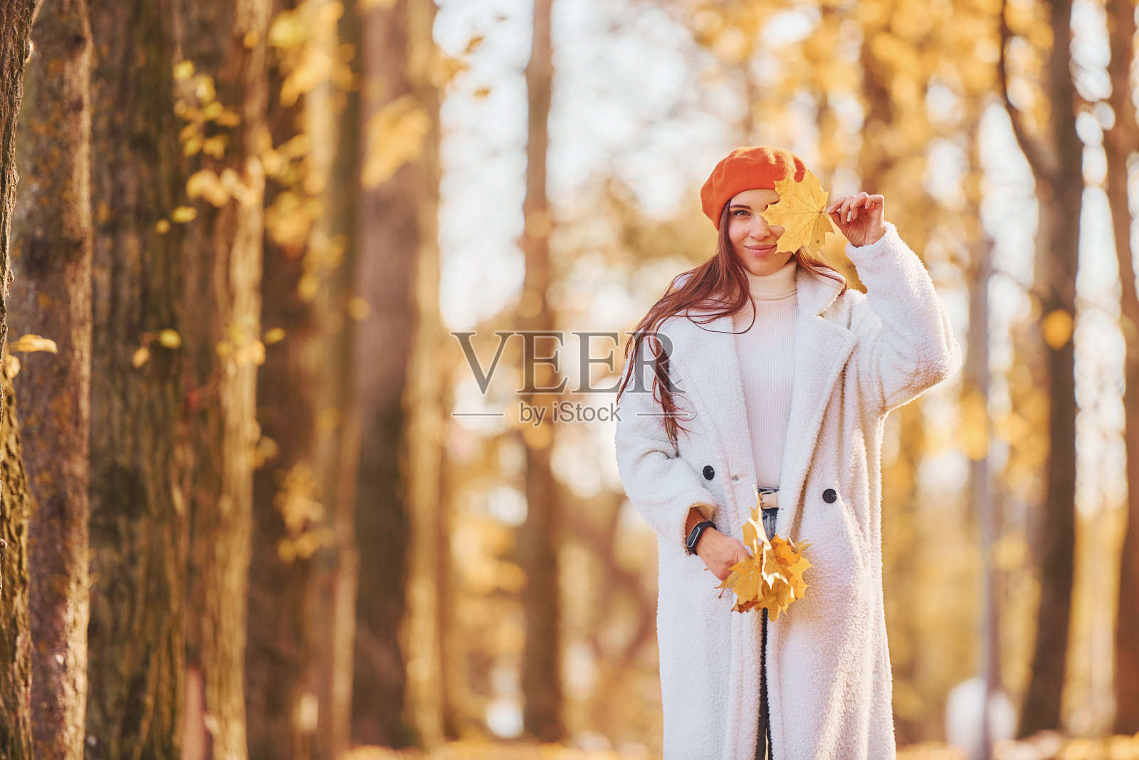 红色贝雷帽。穿着白大褂的女人在秋天的公园里玩耍照片摄影图片