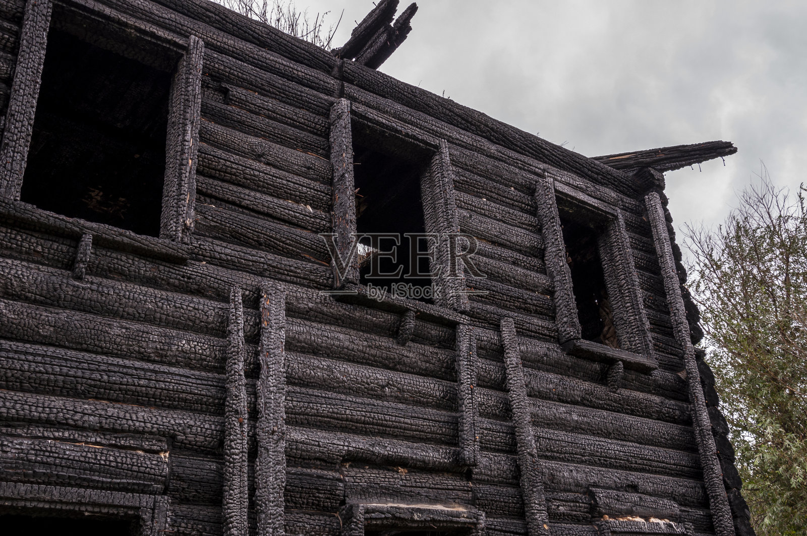 一座被烧毁的木屋映衬着深灰色的天空。大火过后照片摄影图片