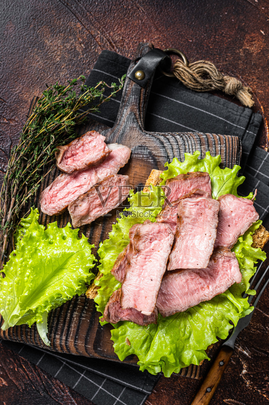 牛排三明治配烤牛肉片，沙拉和蔬菜。黑暗的背景。俯视图照片摄影图片