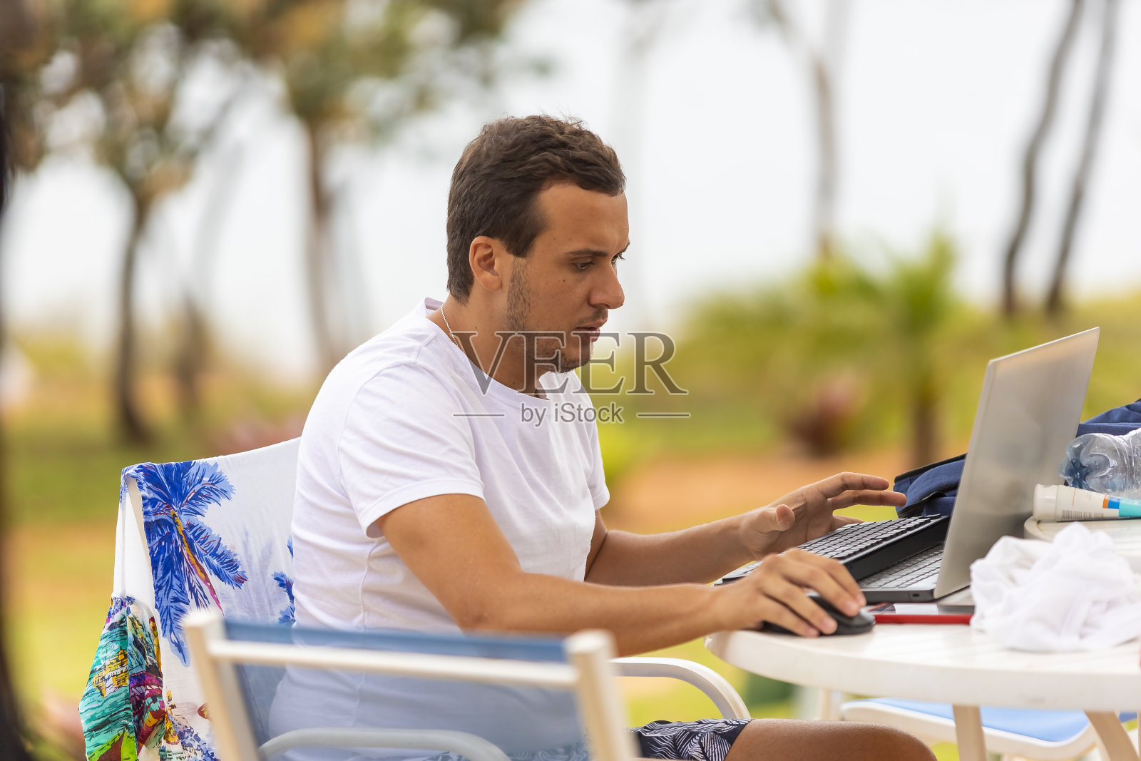 一名男子在沙滩椅上用笔记本电脑工作，模糊的海水背景照片摄影图片