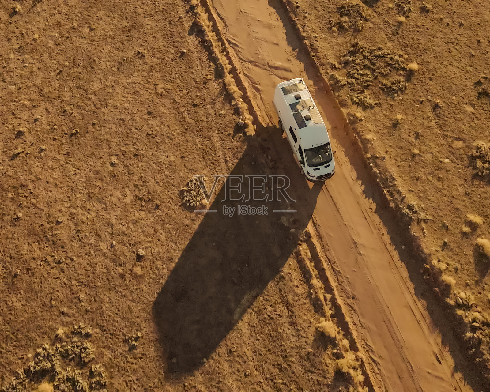 向下俯视的无人机视野白色改装露营车行驶在一条土路上，在犹他州摩押附近的科罗拉多西南部的沙漠山地景观照片摄影图片