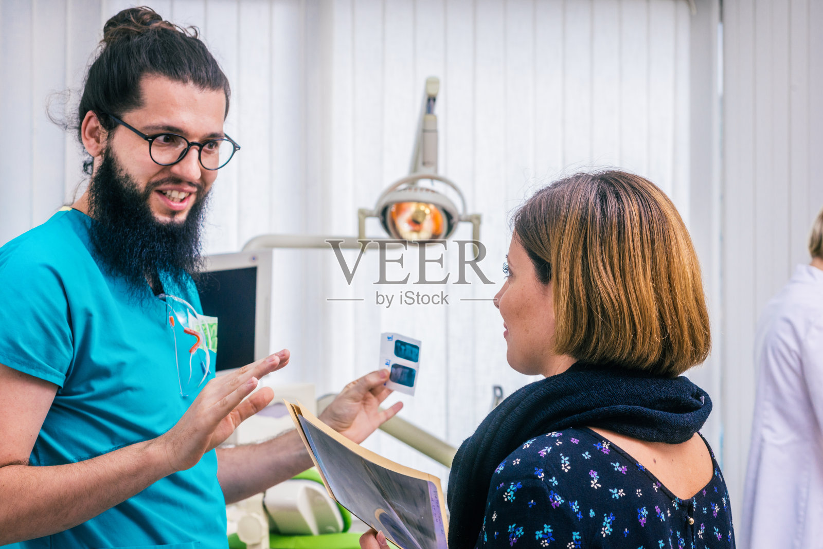 留着胡子的牙医戴着眼镜看着牙科x光扫描，和他的女病人交谈。照片摄影图片