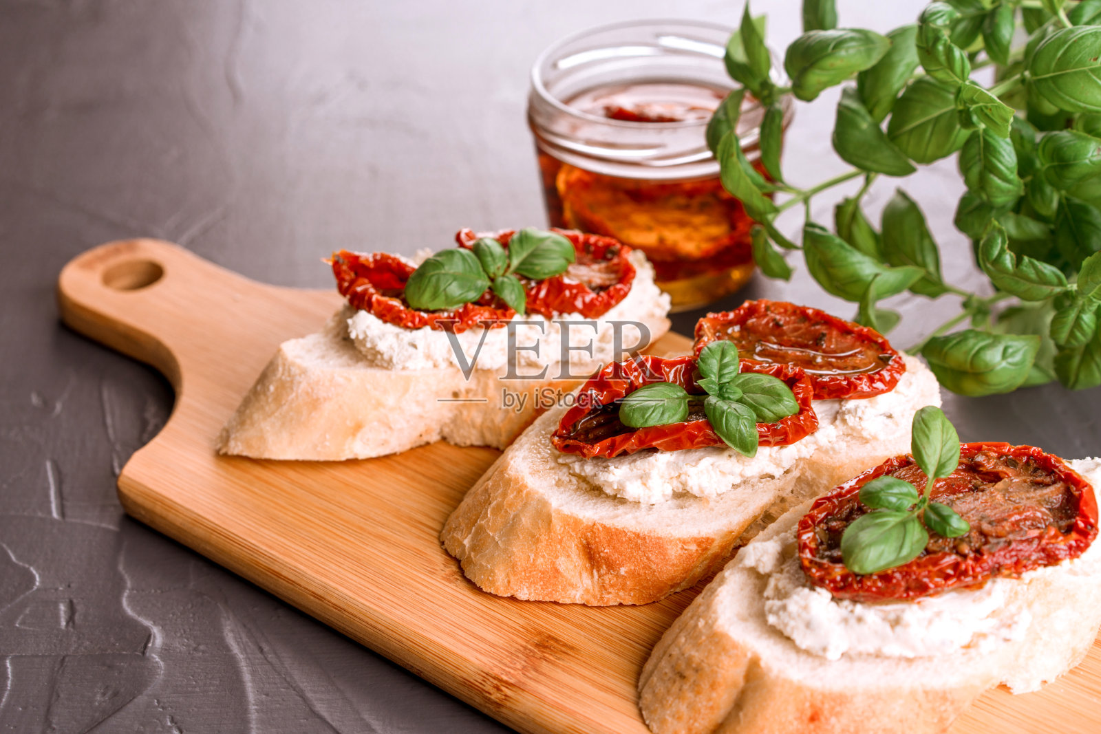 美味的意大利乳清干酪烤面包，晒干的番茄切片，上面放上香草，罗勒，番茄干和橄榄，放在木制的盘子上，深色的桌子背景。经典的开胃菜照片摄影图片