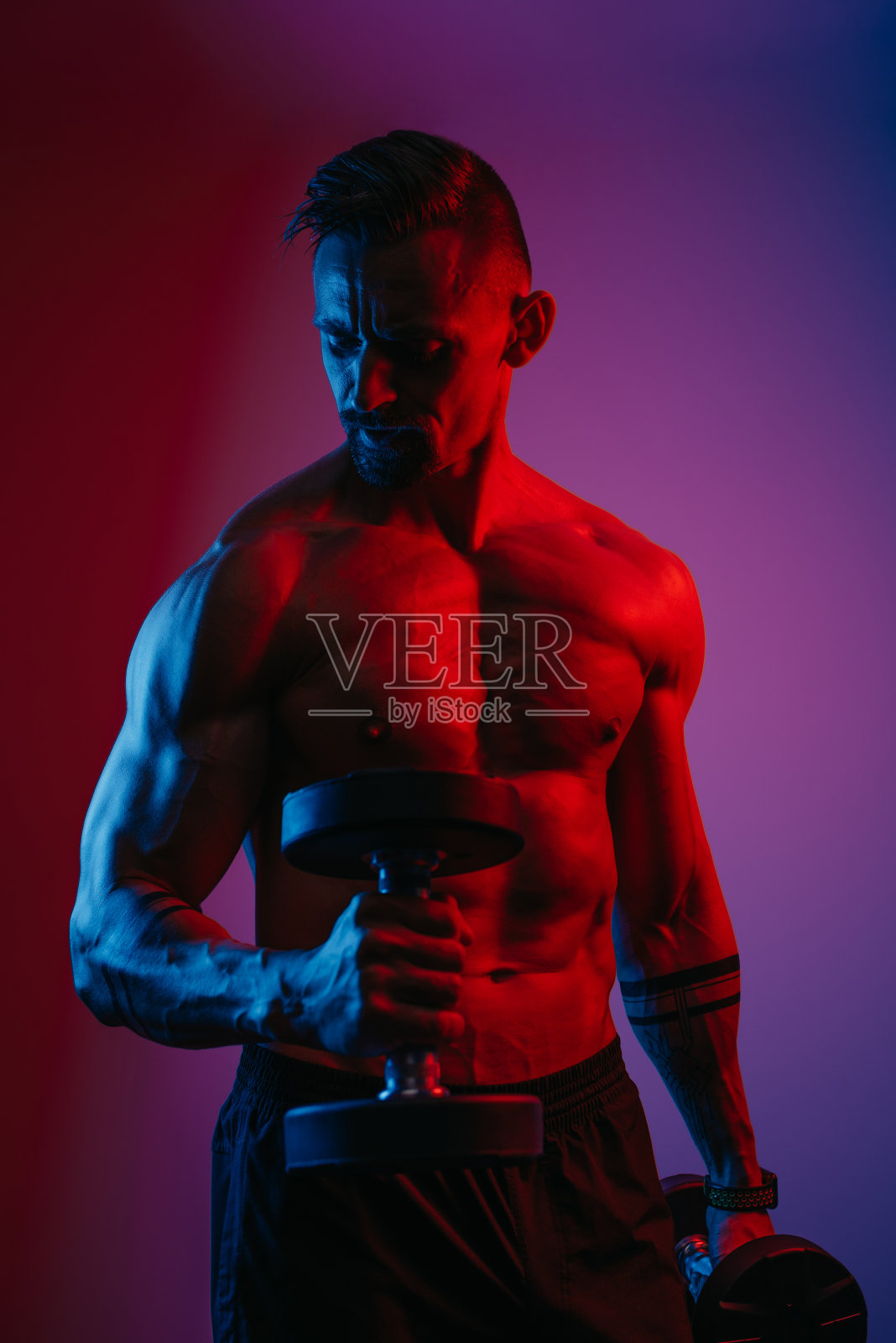 健美运动员在蓝色和红色灯光下用哑铃做二头肌锤卷照片摄影图片