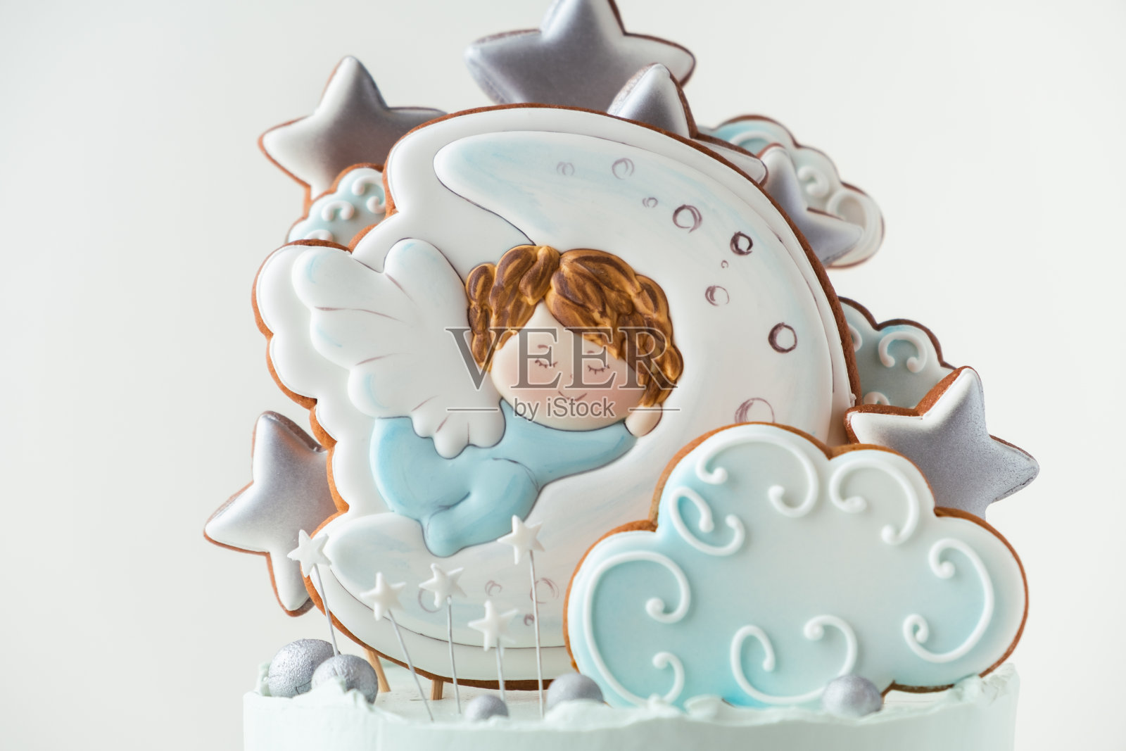 白色背景上装饰着姜饼饼干的蓝奶油芝士糖霜洗礼蛋糕。小天使睡在月亮上。照片摄影图片