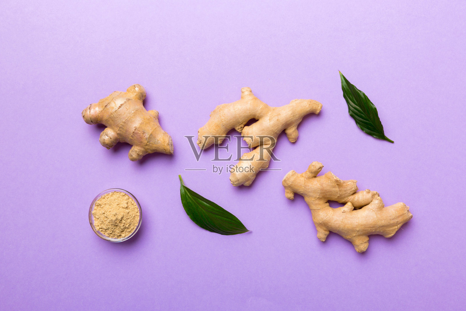 在碗中放入干姜粉，绿色的叶子在有色的背景上。俯视图平铺照片摄影图片