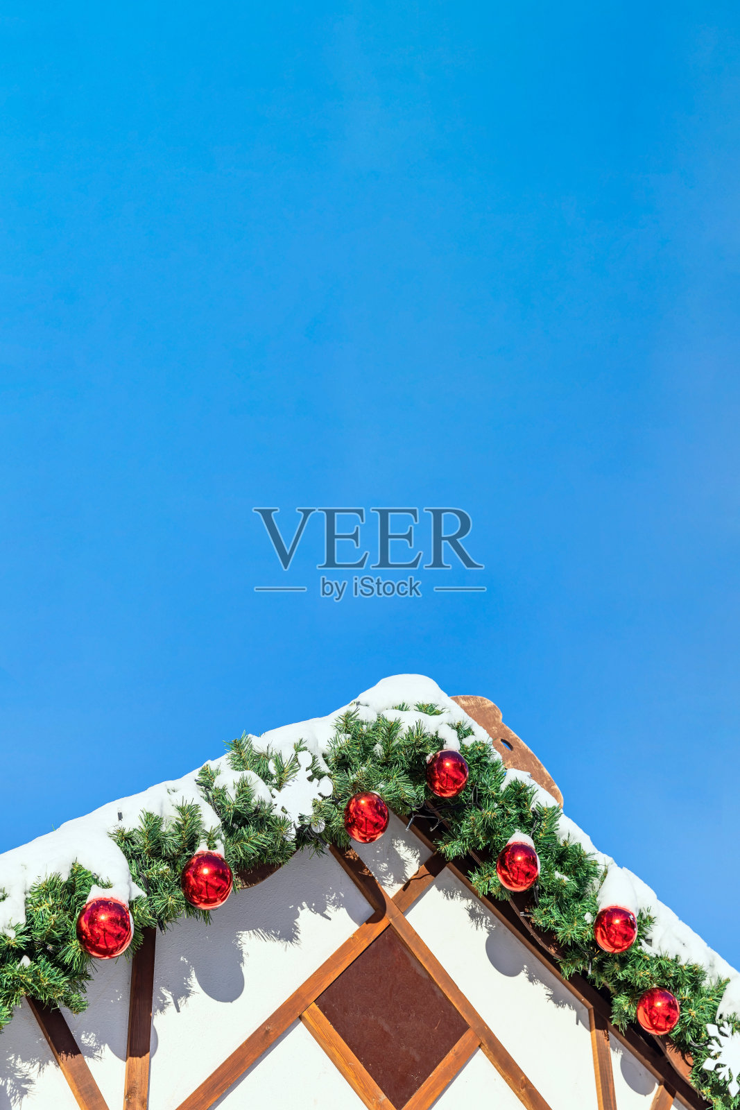 木制的屋顶装饰着圣诞玩具，红色的球，花环树枝覆盖着雪照片摄影图片