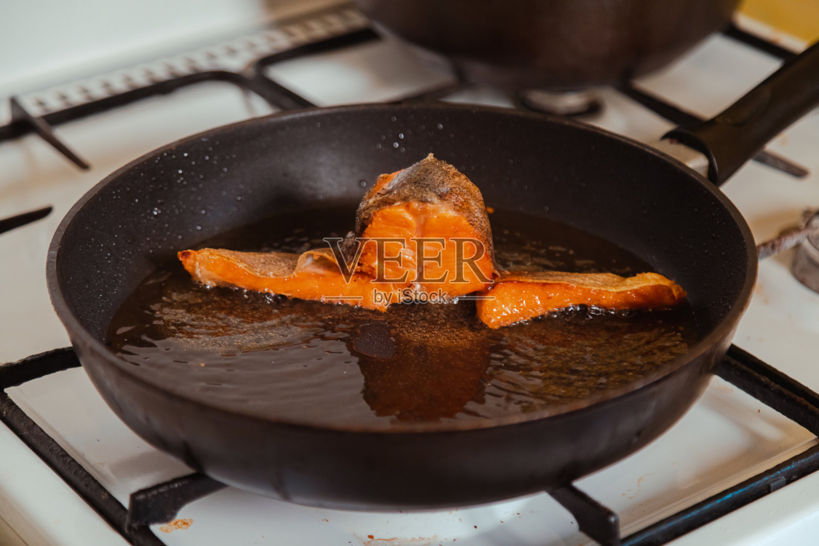 在家里的厨房里，用热油锅煎鲑鱼片照片摄影图片