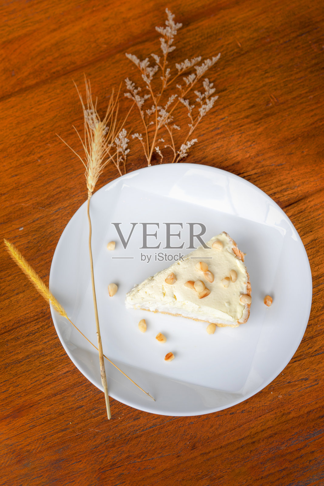 在木桌子上的白色盘子里放着椰子奶油派，上面点缀着澳洲坚果。在阳光下拍摄。照片摄影图片