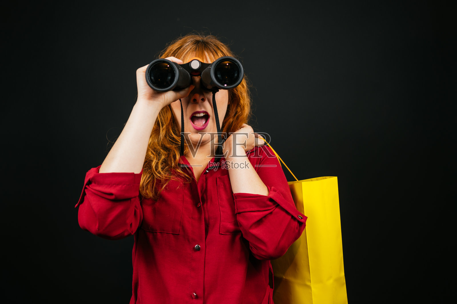 一个白人妇女拿着双筒望远镜和一个购物袋，在黑色雾霭的背景下看着相机照片摄影图片