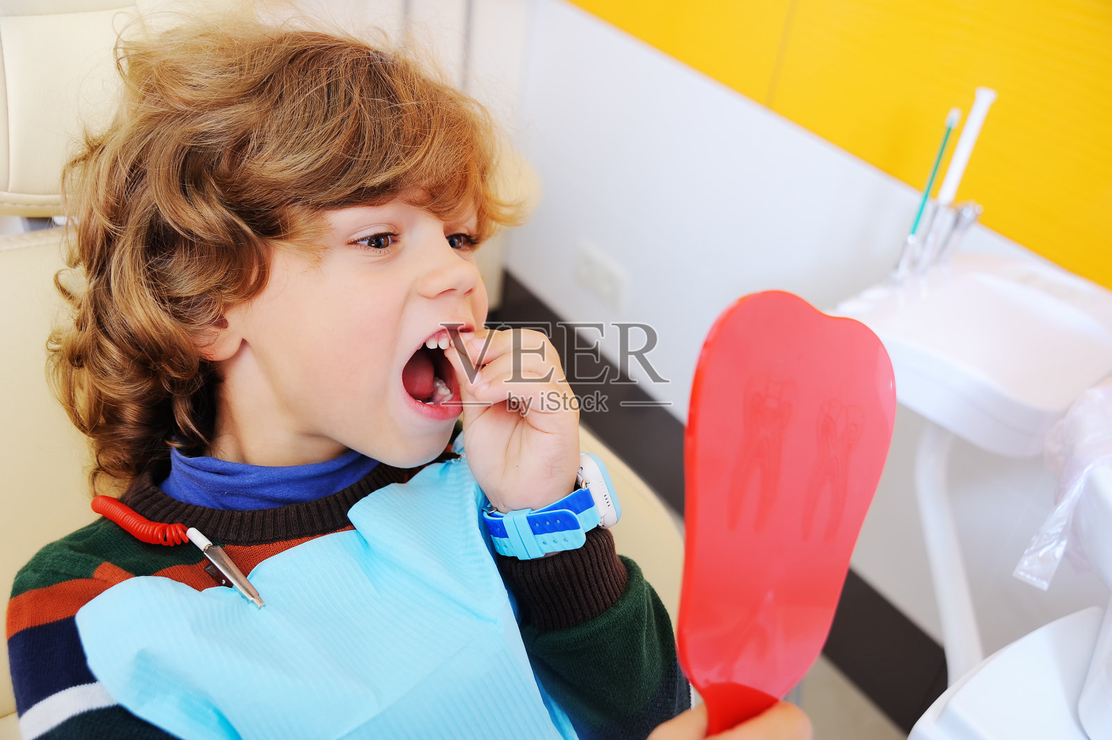 卷曲头发的孩子在牙科椅上放纵地做鬼脸照片摄影图片