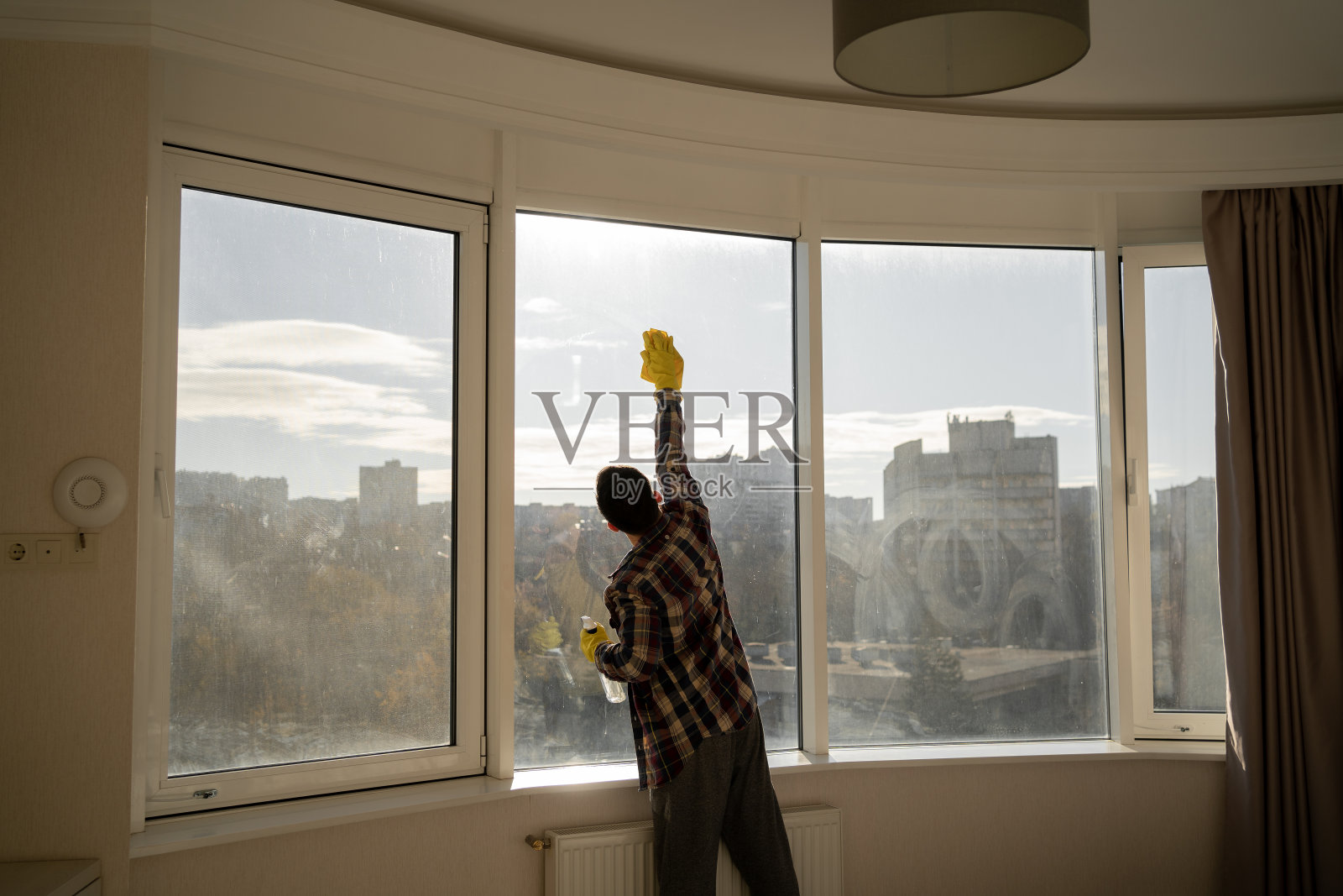 男人在家擦窗户，便服穿衬衫，黄色橡胶手套，家居清洁概念。照片摄影图片