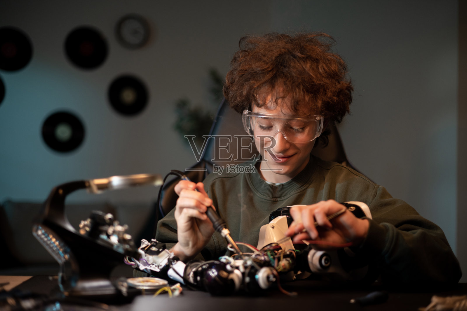 一头卷发的男孩戴着护目镜，花时间培养爱好。孩子练习手工技能，焊接从机器人上取下的电子产品，修理玩具照片摄影图片