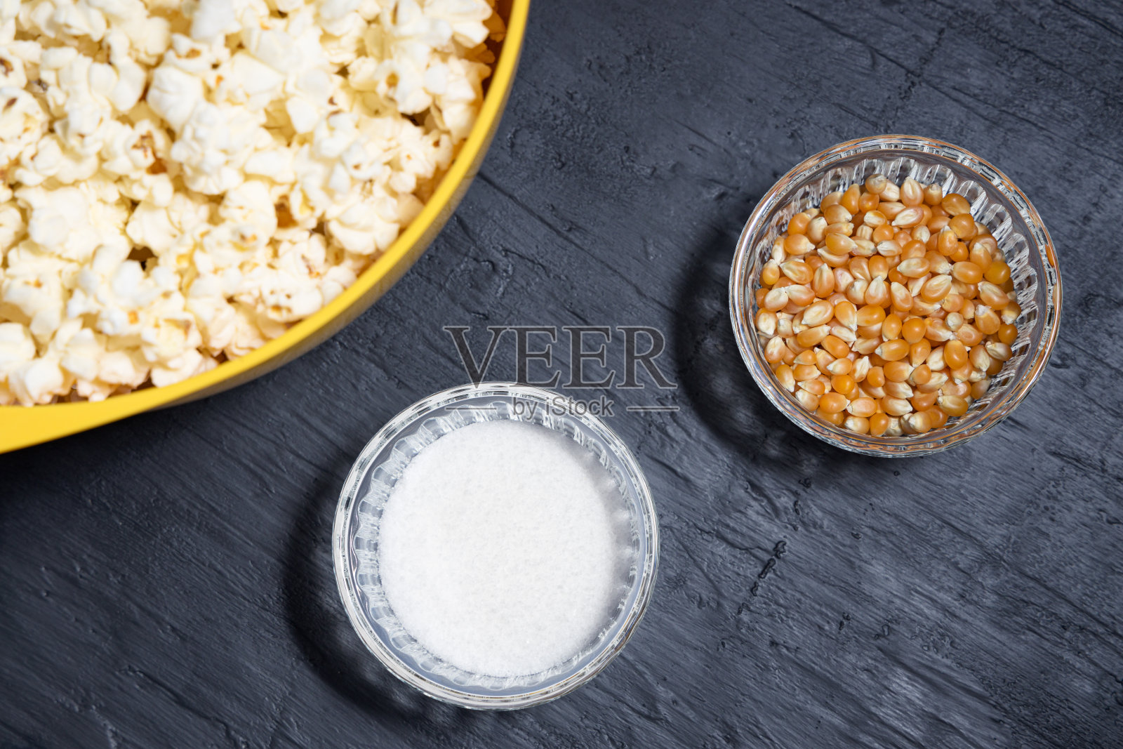 爆米花放在一个黄色的碗里，旁边放着玉米粒和盐照片摄影图片