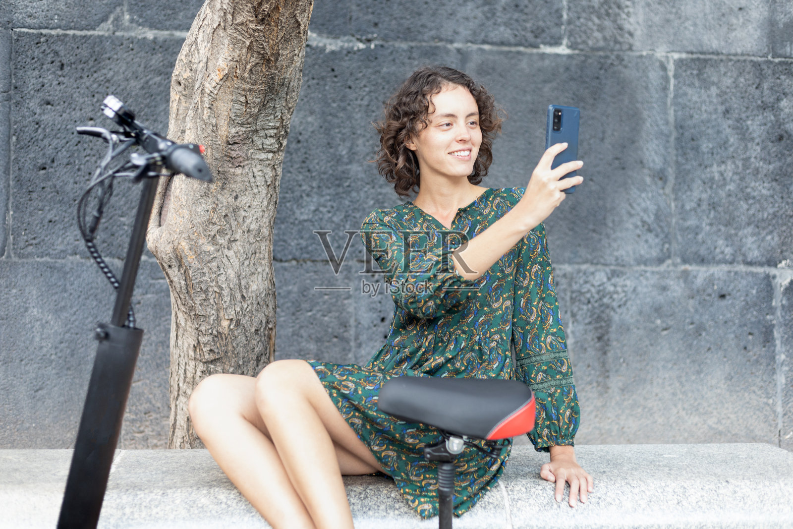 穿着绿色裙子的女孩在电动车旁拍照。照片摄影图片