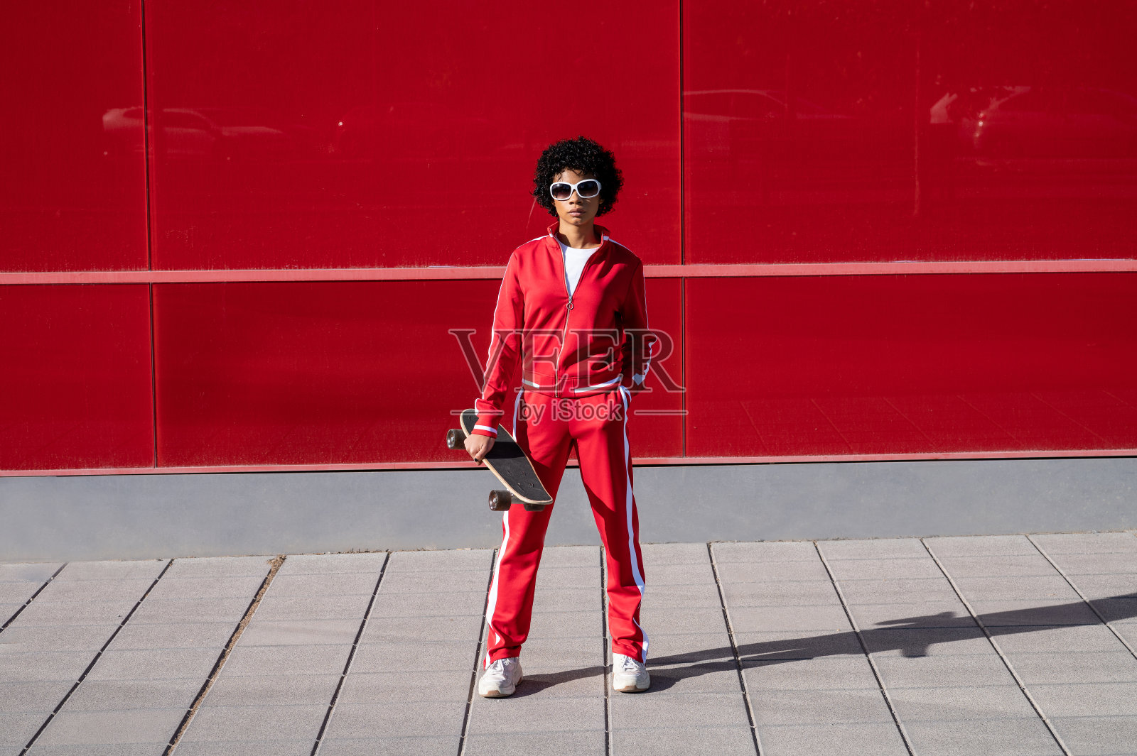 年轻的非裔美国妇女，短发，运动服，在红色的墙上滑着滑板照片摄影图片