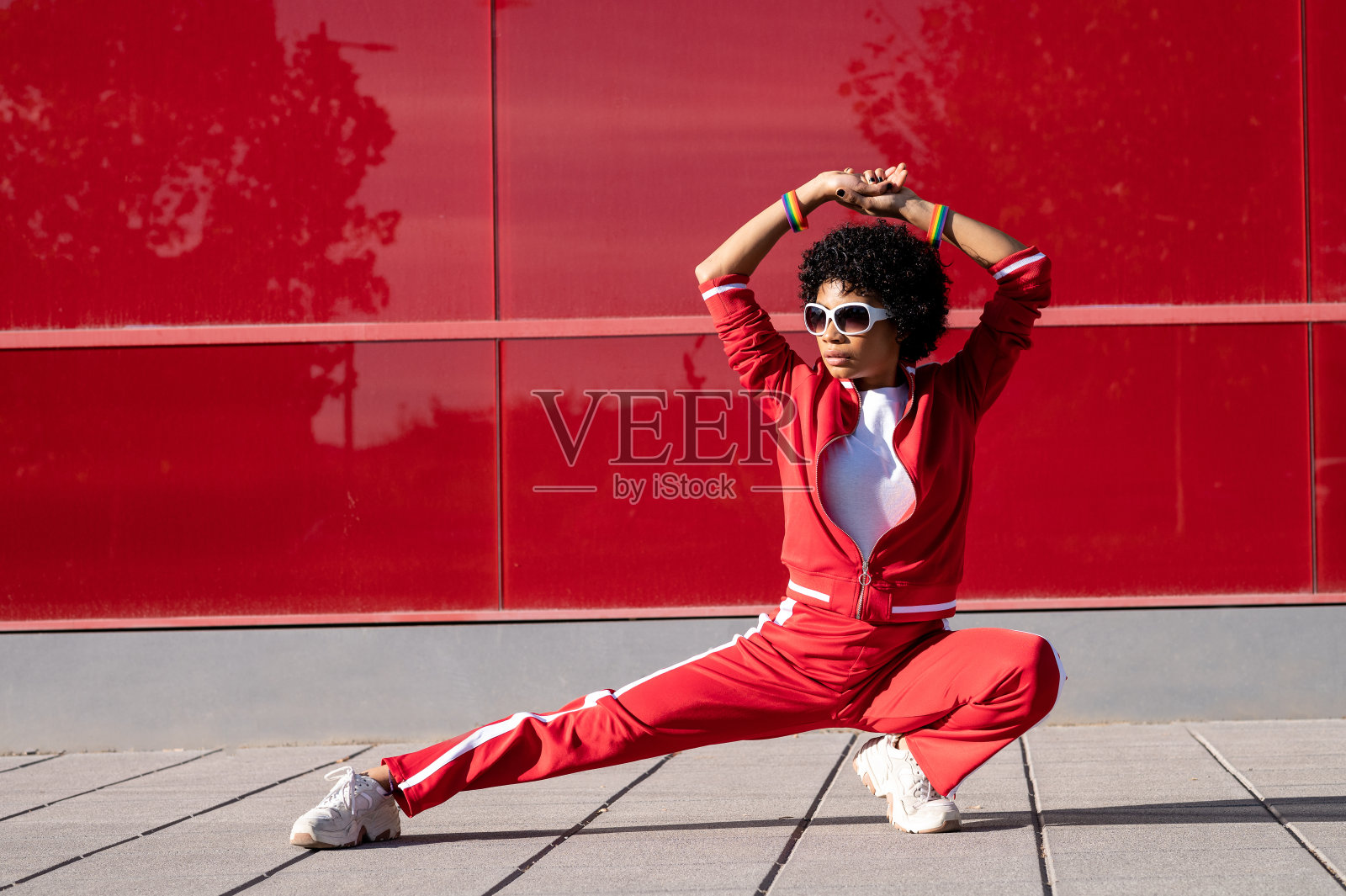年轻的非裔美国妇女，短发，运动服，在一个阳光明媚的日子里挂在红色的墙上照片摄影图片