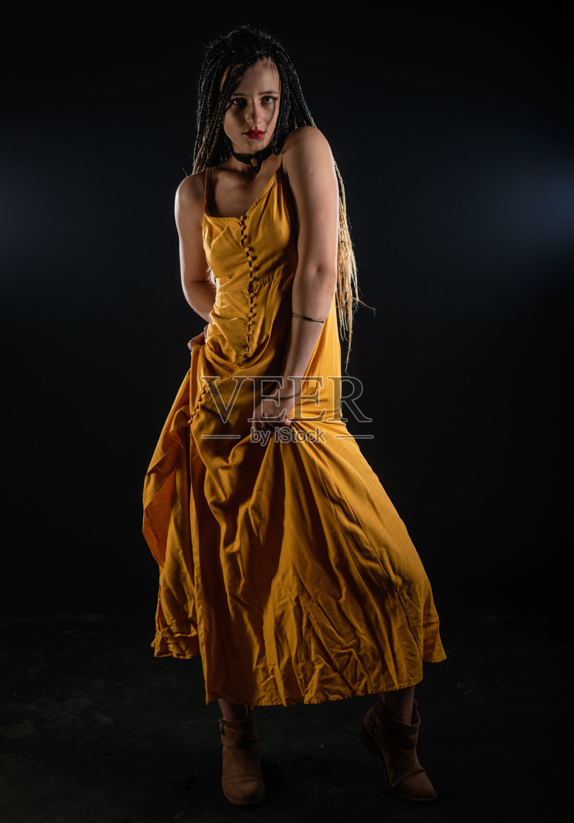 神秘的古代皇后女神穿着黄色连衣裙在一个孤立的黑色工作室背景。女性女权主义者，戴着辫子，在摄影棚里摆姿势。照片摄影图片