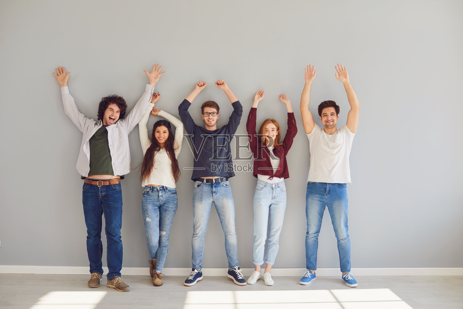 一群穿着休闲服装的青年学生站在灰色的背景下高兴地举起了手。照片摄影图片