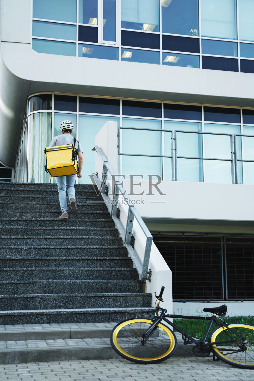 快递员带着保温袋，骑完自行车上楼梯。照片摄影图片