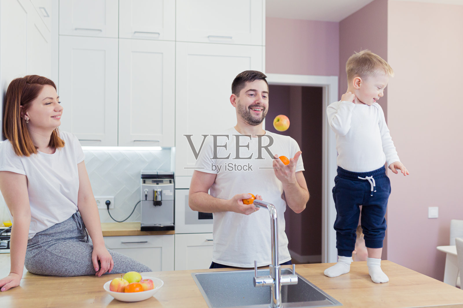 年轻的一家人在厨房里准备新鲜的水果做早餐，孩子们帮着父母，笑着，玩得很开心照片摄影图片