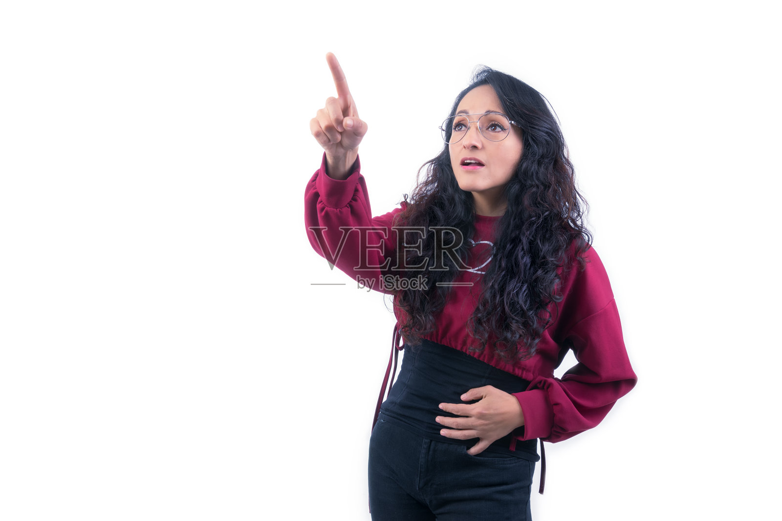 漂亮的拉丁裔西班牙妇女，长着浓密的头发，戴着白色的眼镜，在室内做着表情和手势，用一只手和手指指着，笑着，快乐，好奇和高兴照片摄影图片