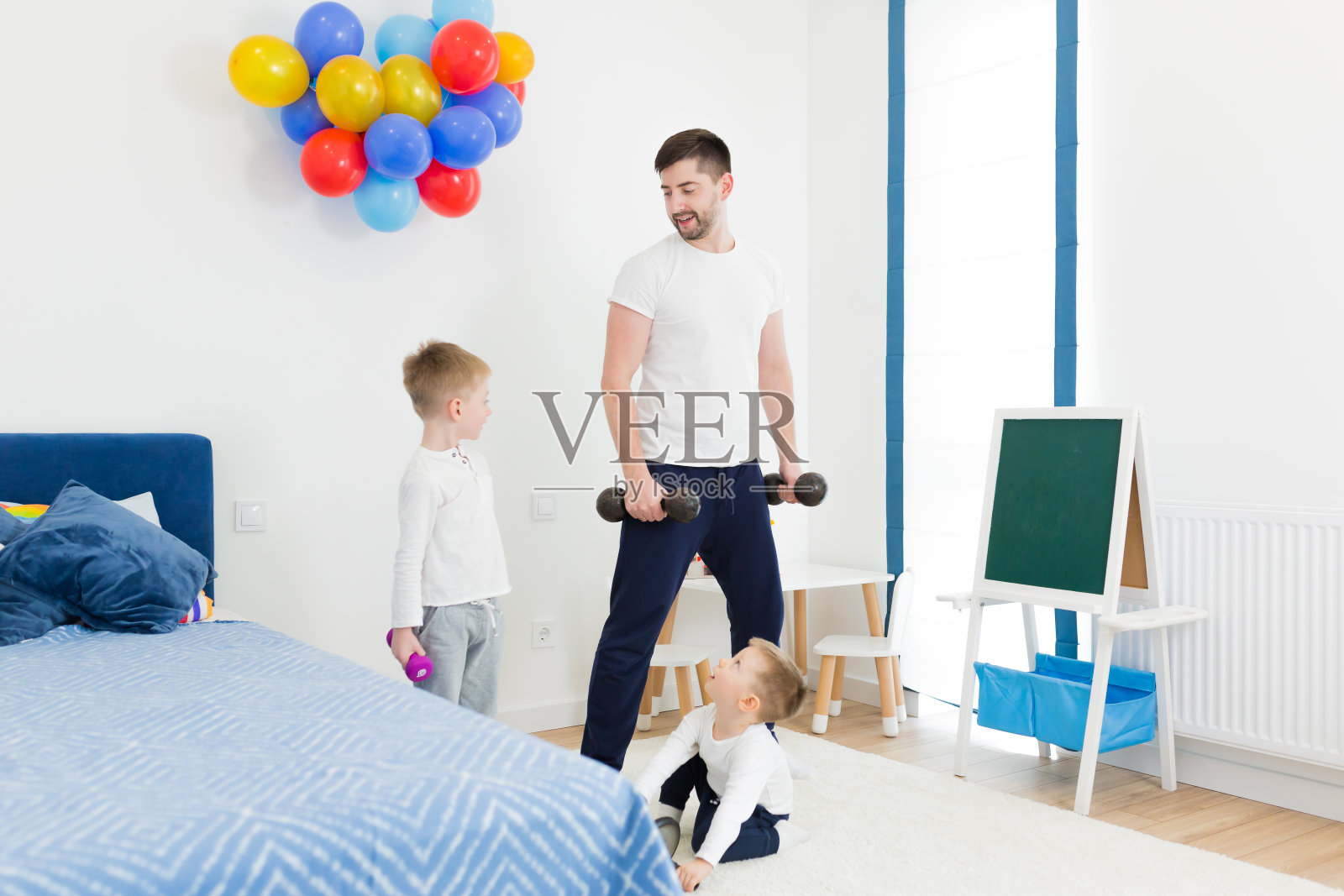 年轻的父亲和两个孩子，两个儿子参加体育运动，用哑铃做练习，在家里的房间里，教，展示，一起玩照片摄影图片