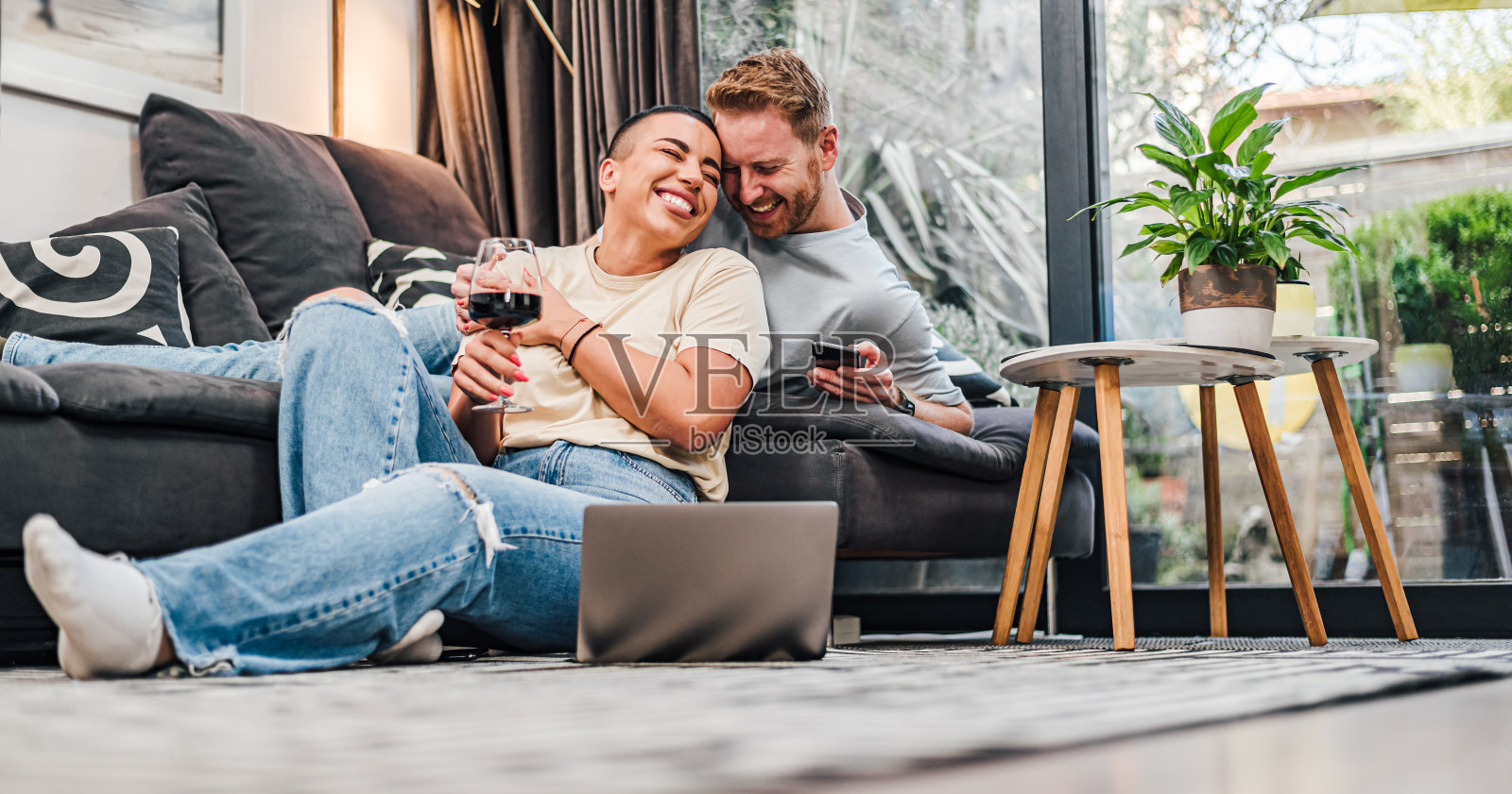 幸福的两个人情侣网上购物年轻人购买网上商店，企业家使用便携式设备支付，夫妇坐在地板上享受购买礼物的笔记本电脑和智能手机在家里。照片摄影图片