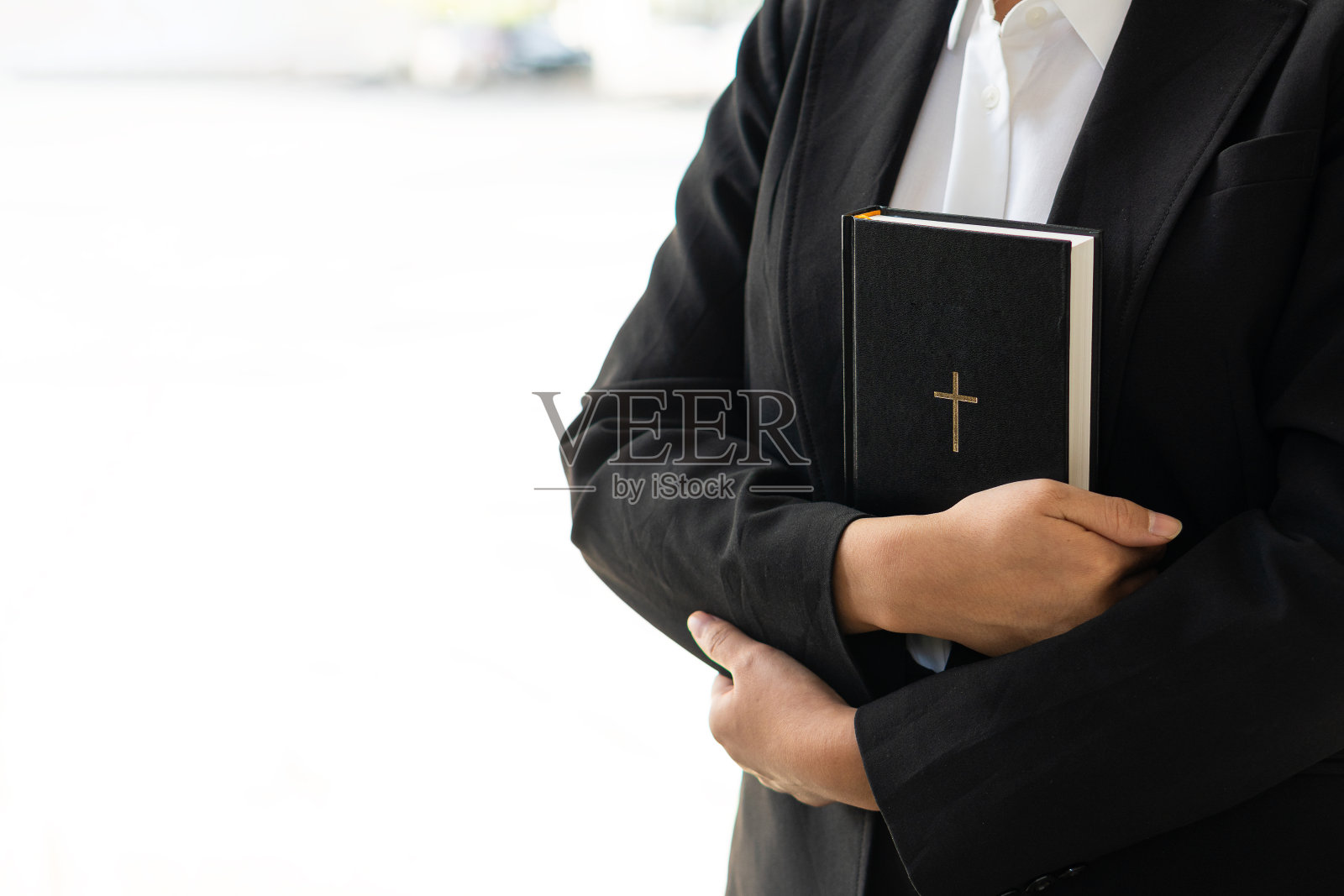 黑色皮革的特写镜头，一个穿着黑色衣服的女人手里拿着一个基督教十字架，她的心里拿着一本圣经。宗教观念和节日照片摄影图片