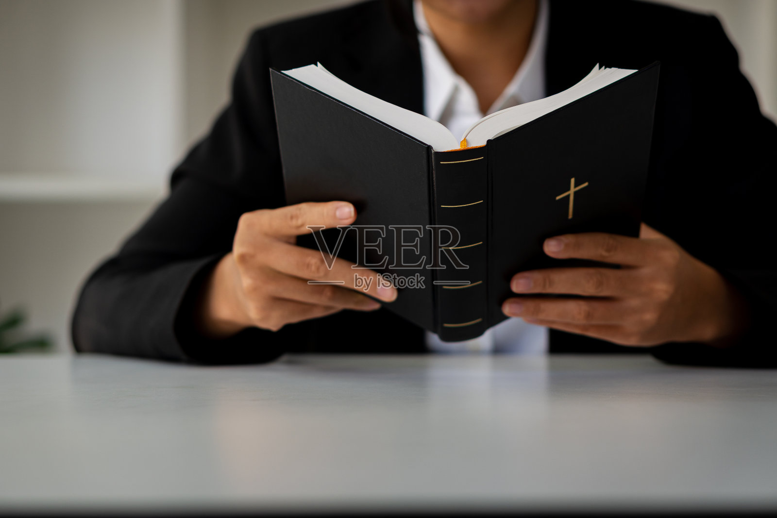 黑色皮革的特写镜头，一个穿着黑色衣服的女人手里拿着一个基督教十字架，她的心里拿着一本圣经。宗教观念和节日照片摄影图片