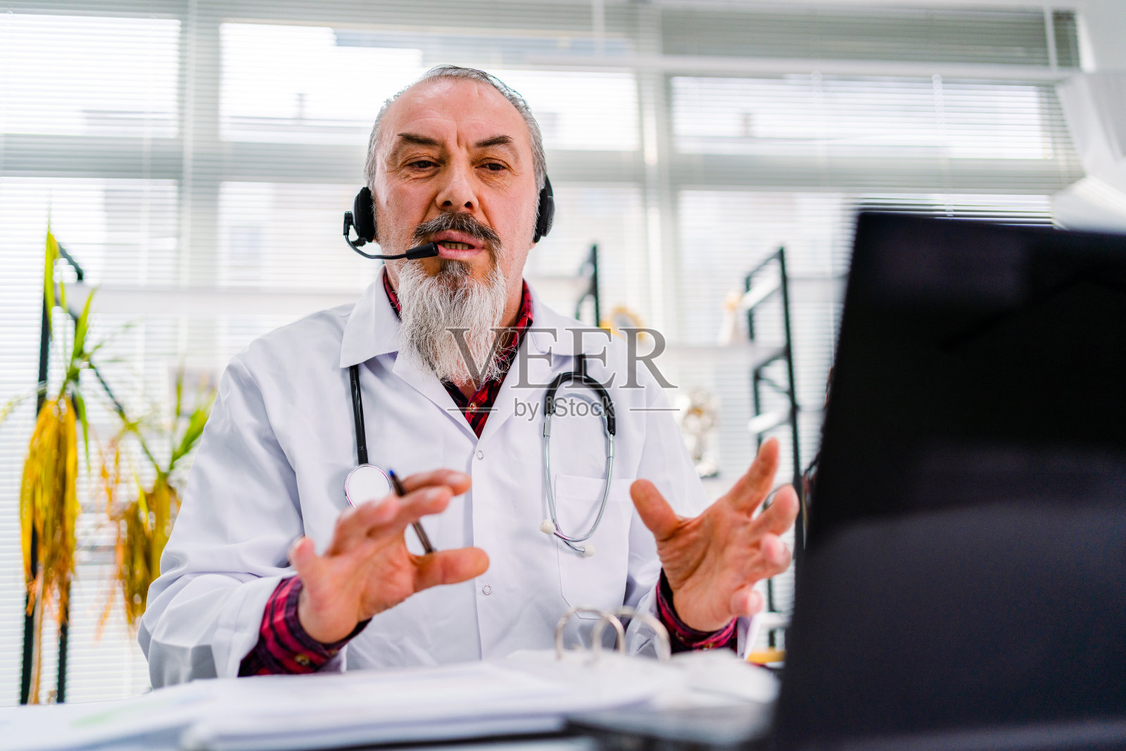 资深医生坐在诊所办公室用笔记本电脑与病人交谈，在线视频网络会诊。远程医疗。照片摄影图片