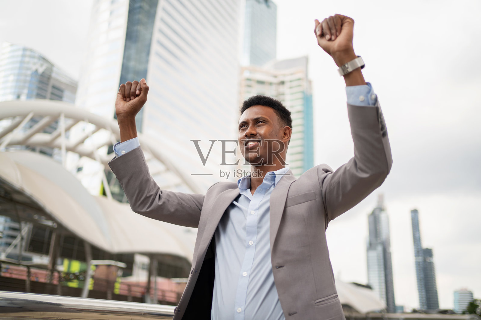 非洲商人穿着西装站在市中心的商业区。举起他的手，微笑。新项目成功。工人拿到奖金后很开心。工作生活理念照片摄影图片