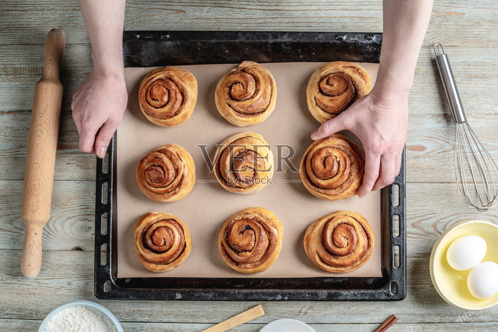 女人的手小心翼翼地从烤盘里拿出新鲜的、温暖的肉桂卷面包。概念美味的自制糕点和舒适的氛围照片摄影图片