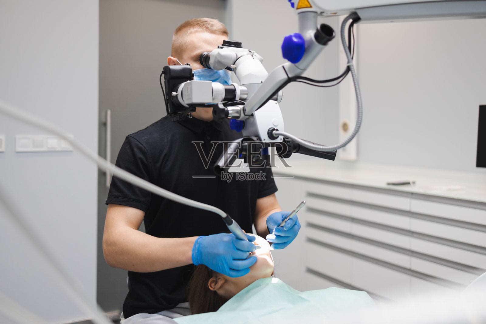 专业的年轻男性牙医用显微镜治疗一位女性病人。牙科的现代技术照片摄影图片