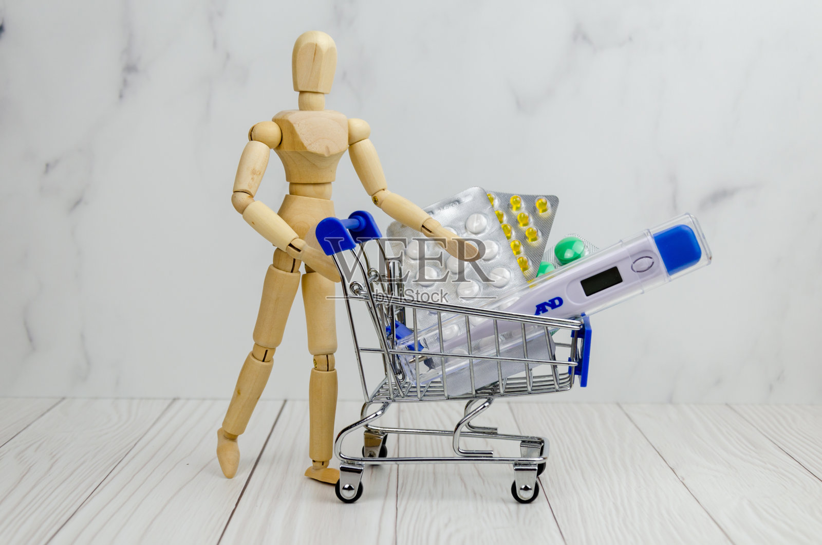木制男子雕像，推着购物车，里面装着药片和温度计。保健概念照片摄影图片