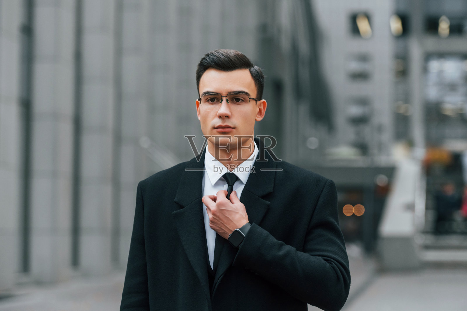 修复领带。穿黑色西装的商人正在城市的户外照片摄影图片