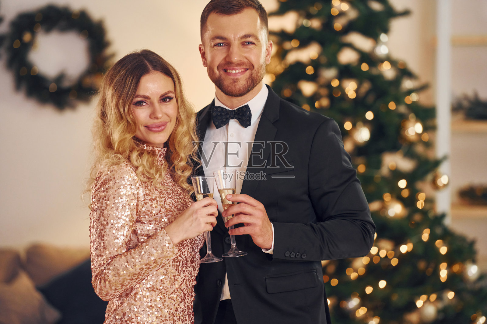 靠着圣诞树站着。幸福的夫妇在室内举行新年聚会照片摄影图片
