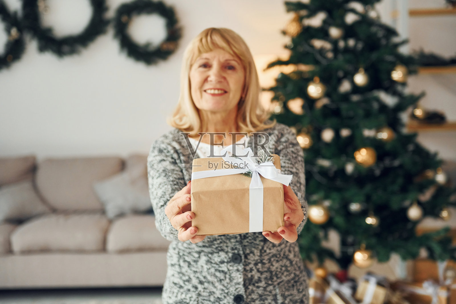 站在圣诞树旁。金发的老女人在家照片摄影图片