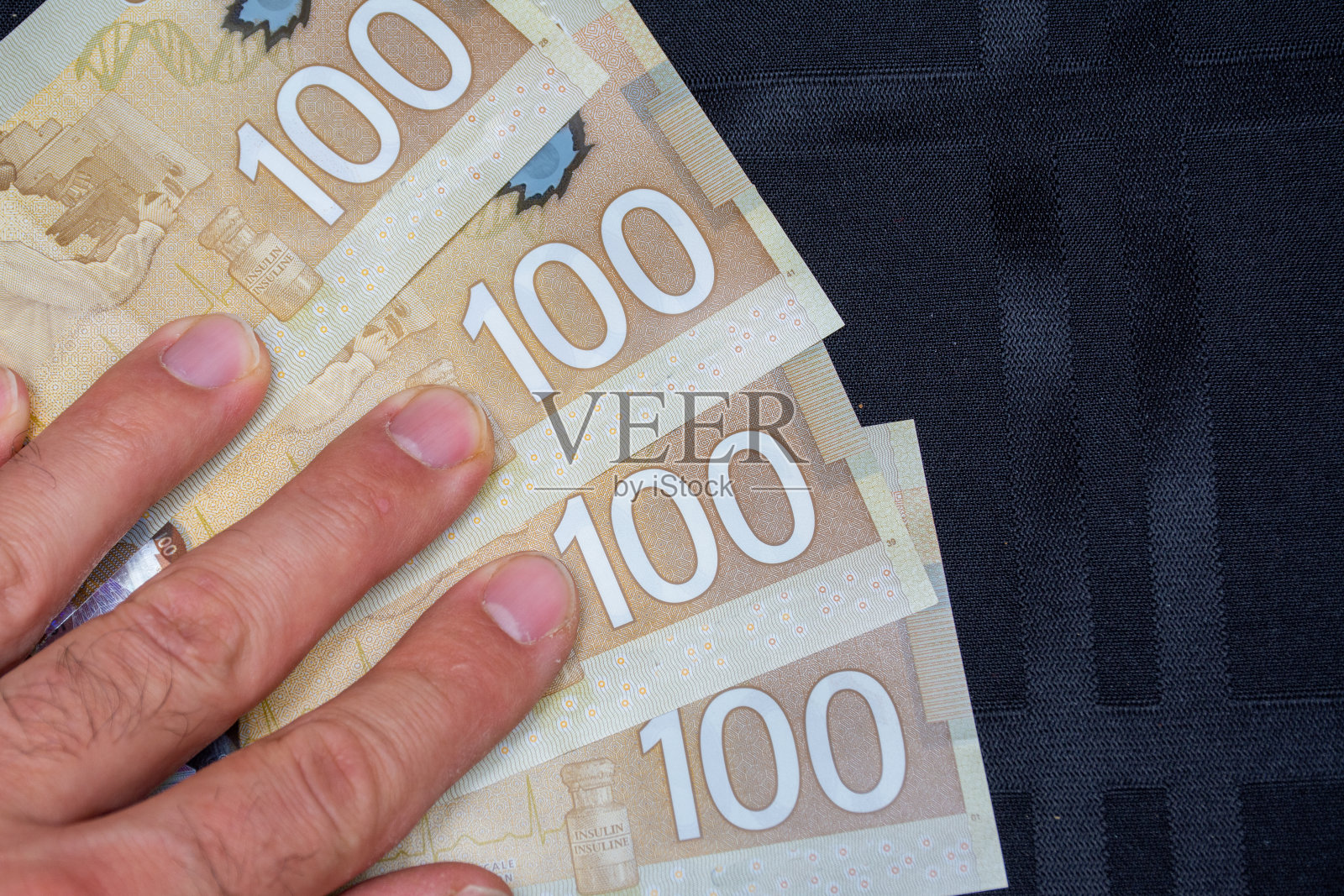 近距离的棕色加拿大百(100)美元与手黑色背景和复制空间。照片摄影图片