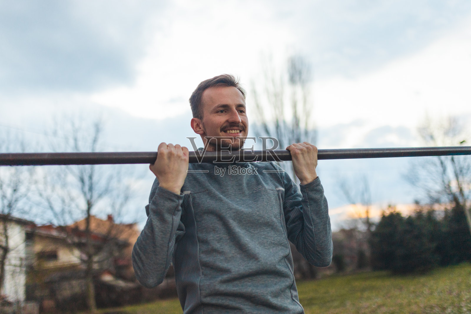 年轻的男性运动员在户外的体操杠上拉着自己照片摄影图片