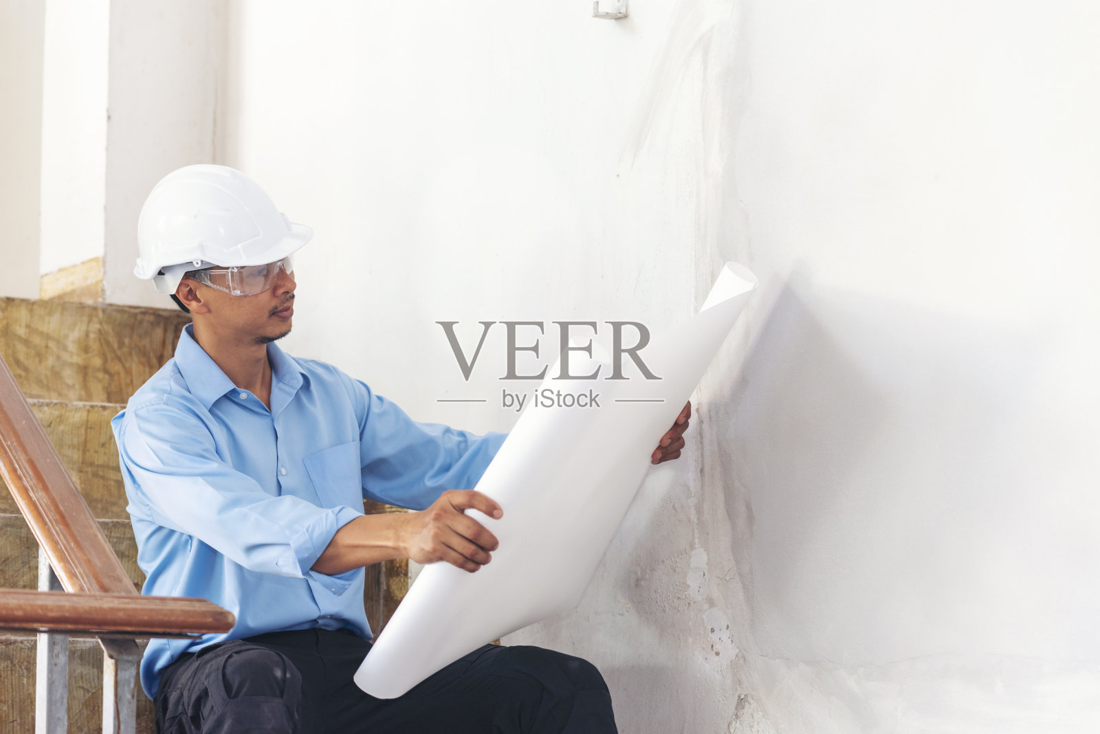 建筑工程人员持图纸，身穿蓝色衬衫安全白色安全帽在建筑工地工业工人。建筑人工程师土木工人看蓝图房地产概念照片摄影图片