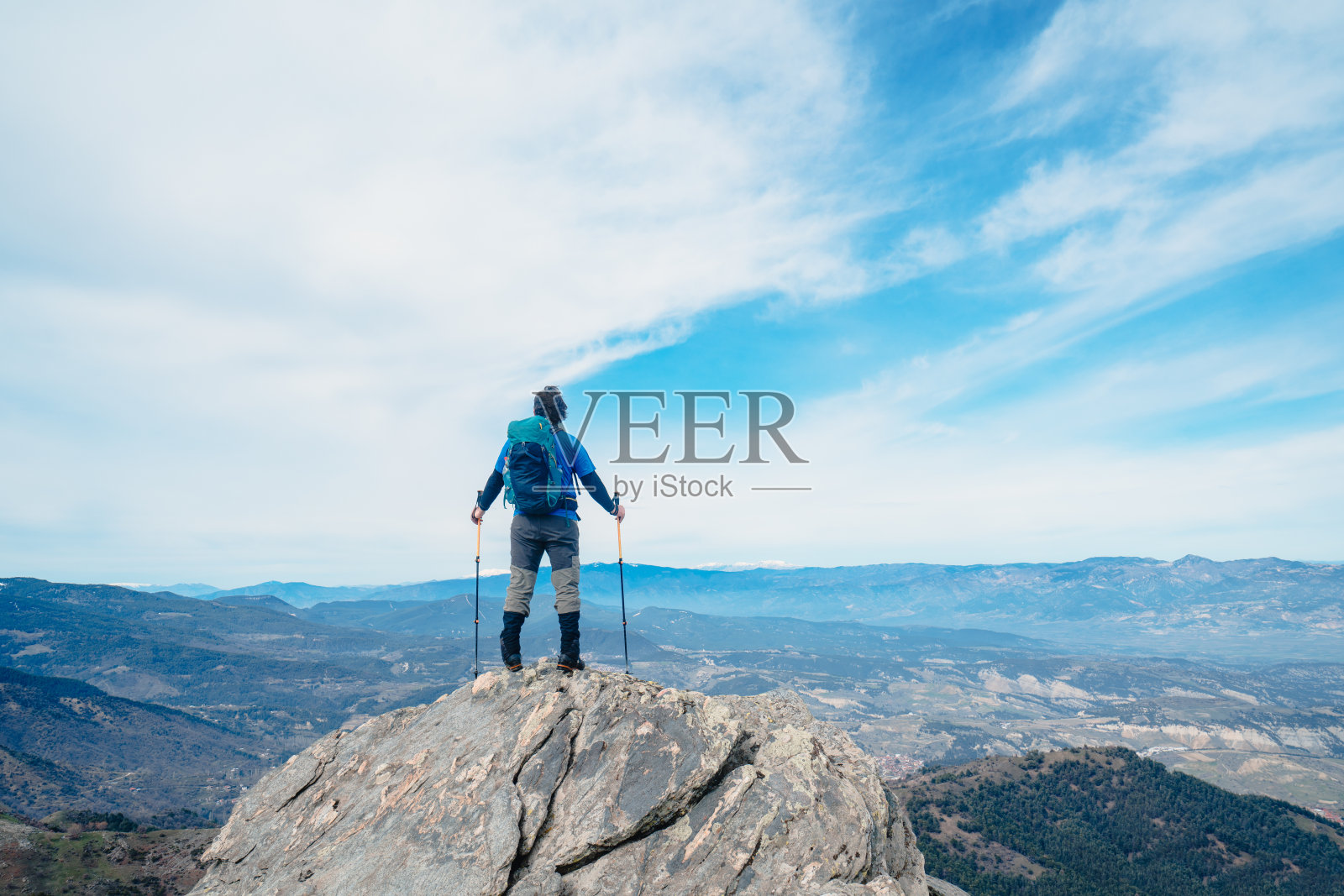 背景摄影师登山运动员是看风景，而持有登山杆在一个岩石山的顶峰。照片摄影图片