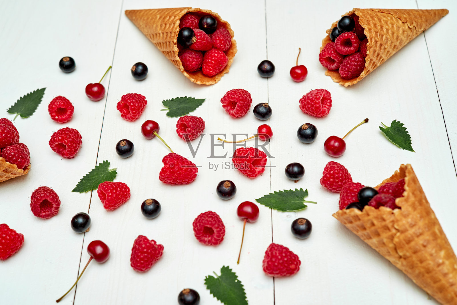 熟透的甜树莓，樱桃和黑加仑在冰淇淋华夫筒，复制空间。新鲜浆果在白色木材背景。夏日与健康饮食理念照片摄影图片