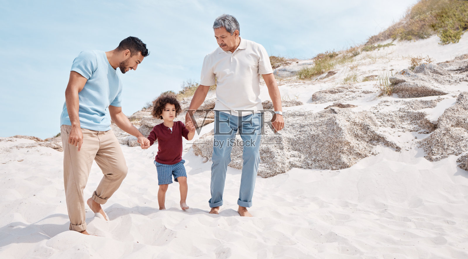 拍摄的是一个小男孩和他的父亲、祖父在海滩上照片摄影图片